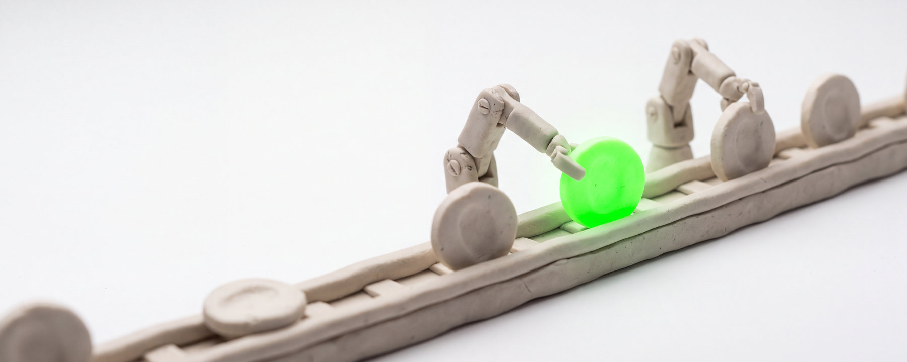 Clay model of a rail carrying coins, handed forward by robot arms, with one coin lit green.